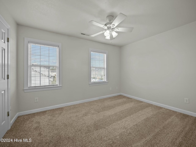 carpeted spare room featuring a wealth of natural light and ceiling fan