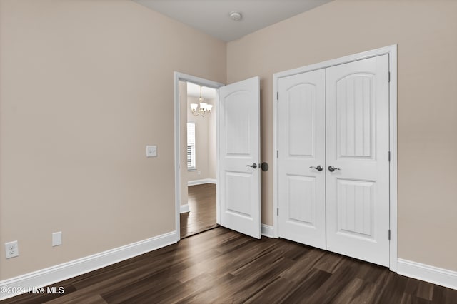 unfurnished bedroom with a closet, a chandelier, and dark hardwood / wood-style floors