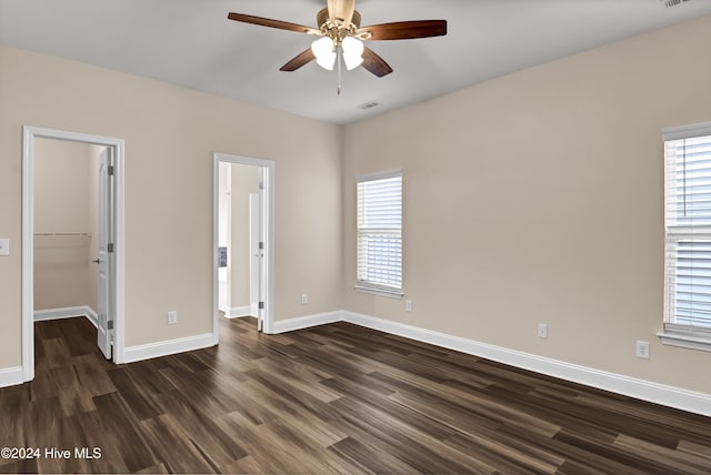 unfurnished bedroom featuring a spacious closet, a closet, ceiling fan, and dark wood-type flooring