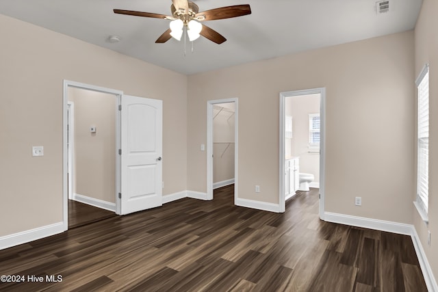 unfurnished bedroom with a walk in closet, ensuite bathroom, ceiling fan, dark wood-type flooring, and a closet