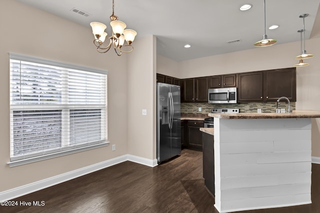 kitchen with kitchen peninsula, appliances with stainless steel finishes, hanging light fixtures, and dark wood-type flooring