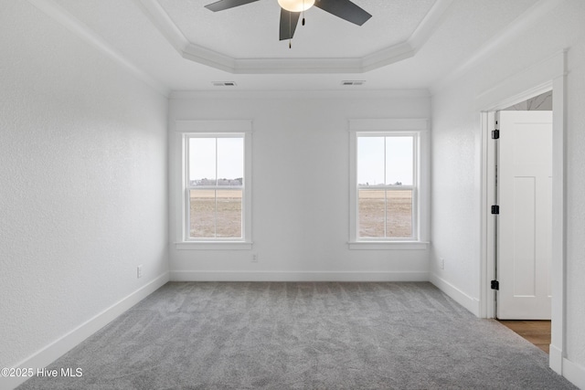 carpeted empty room with baseboards, visible vents, a tray ceiling, and crown molding