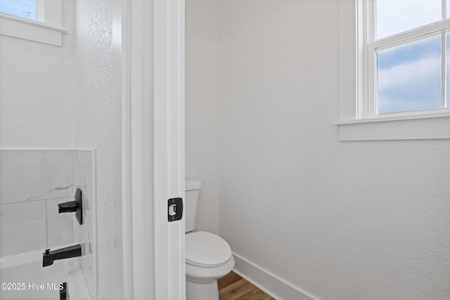 bathroom with toilet, baseboards, wood finished floors, and a textured wall