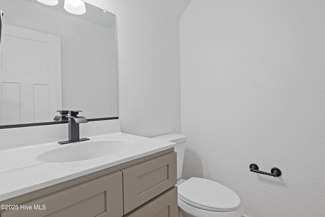 bathroom featuring a textured wall, vanity, and toilet