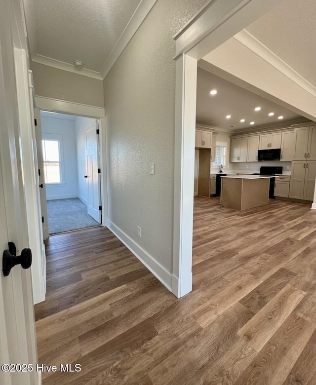 hallway featuring ornamental molding, a textured wall, baseboards, and wood finished floors