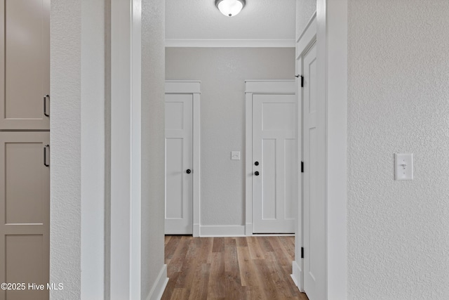 hallway featuring baseboards, a textured wall, ornamental molding, wood finished floors, and a textured ceiling