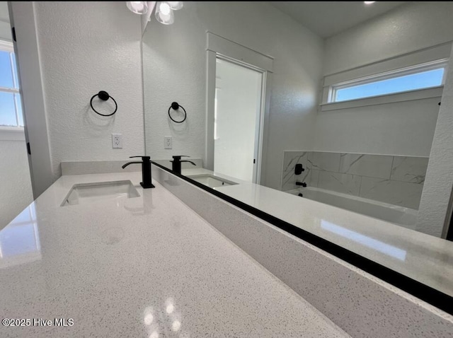 full bathroom with double vanity, a garden tub, and a sink