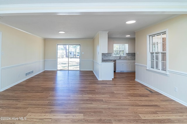 unfurnished living room with visible vents, wood finished floors, a wainscoted wall, and a sink