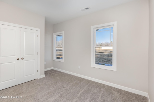 unfurnished bedroom with multiple windows, light carpet, and a closet