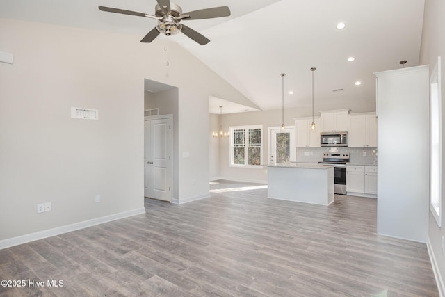 kitchen featuring appliances with stainless steel finishes, hanging light fixtures, white cabinets, a kitchen island, and decorative backsplash