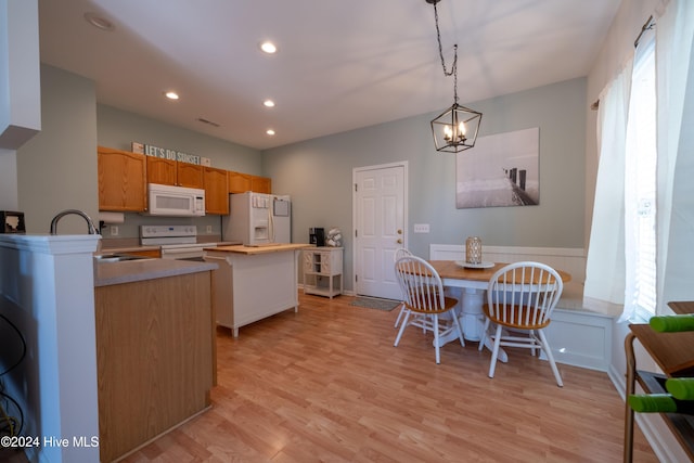 kitchen with light wood-type flooring, white appliances, hanging light fixtures, and a wealth of natural light