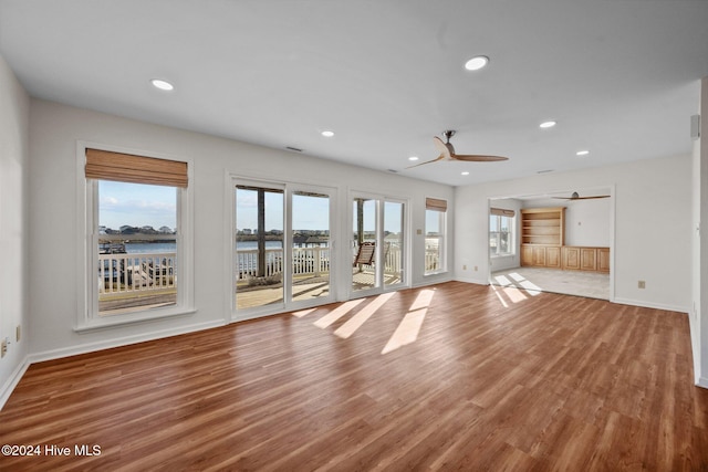 unfurnished living room with hardwood / wood-style floors, ceiling fan, and a water view