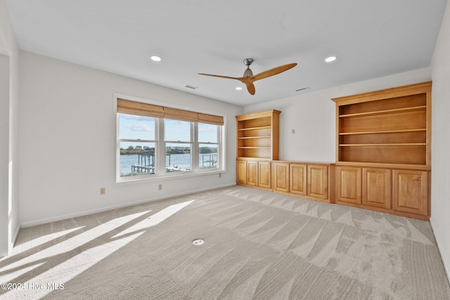 unfurnished living room with a water view, ceiling fan, and light colored carpet