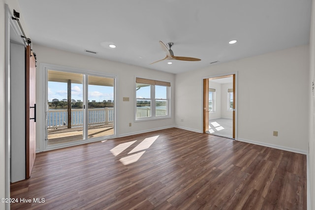 empty room featuring a barn door, a water view, dark hardwood / wood-style floors, and ceiling fan