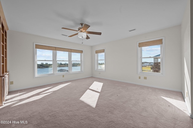 carpeted empty room with plenty of natural light, ceiling fan, and a water view