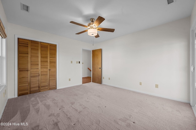 unfurnished bedroom featuring ceiling fan, light colored carpet, and a closet