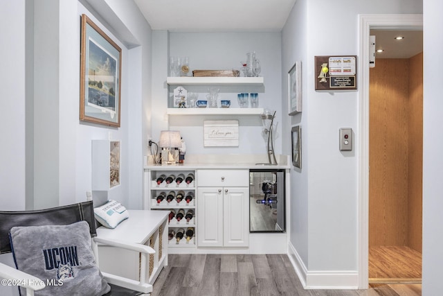 bar featuring white cabinets, elevator, and light hardwood / wood-style flooring