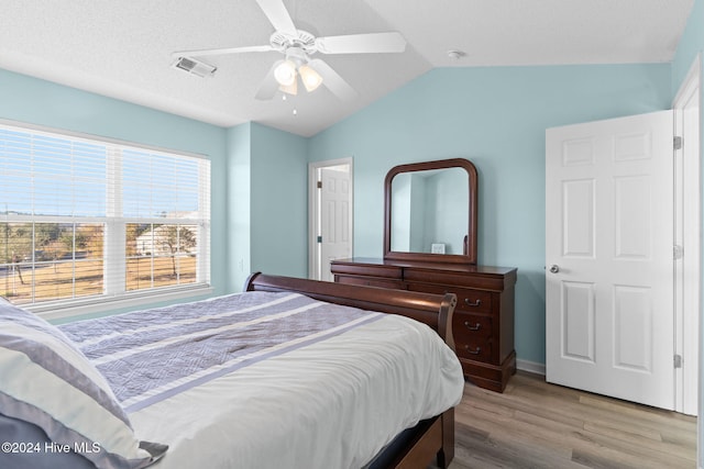 bedroom with ceiling fan, light wood-type flooring, a textured ceiling, and lofted ceiling