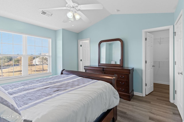 bedroom featuring a walk in closet, vaulted ceiling, ceiling fan, wood-type flooring, and a closet