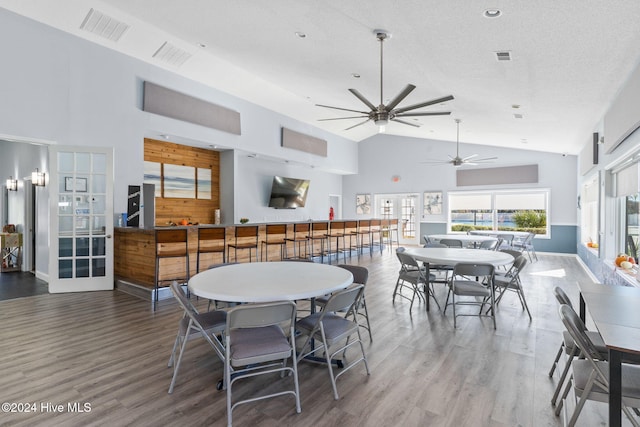 dining space with ceiling fan, french doors, high vaulted ceiling, wood-type flooring, and a textured ceiling