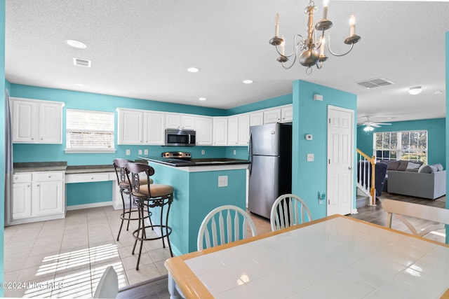 kitchen with white cabinets, ceiling fan with notable chandelier, stainless steel appliances, and hanging light fixtures