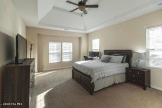 carpeted bedroom with ceiling fan and a tray ceiling