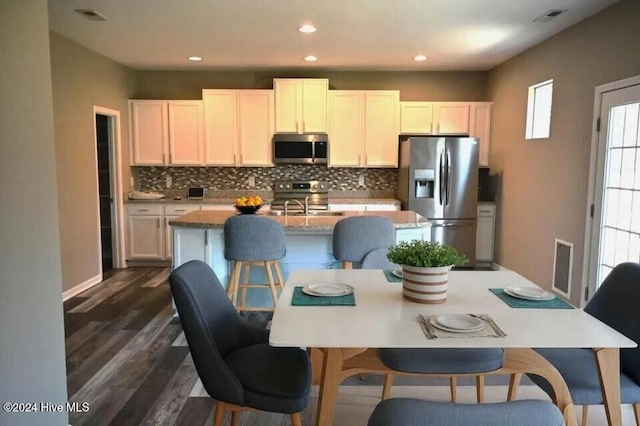 kitchen featuring white cabinetry, dark hardwood / wood-style flooring, backsplash, an island with sink, and appliances with stainless steel finishes