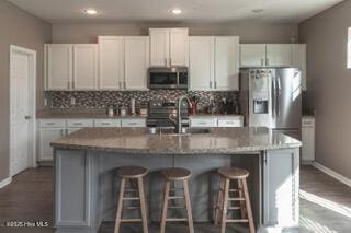 kitchen with sink, white cabinetry, a center island with sink, stainless steel appliances, and decorative backsplash