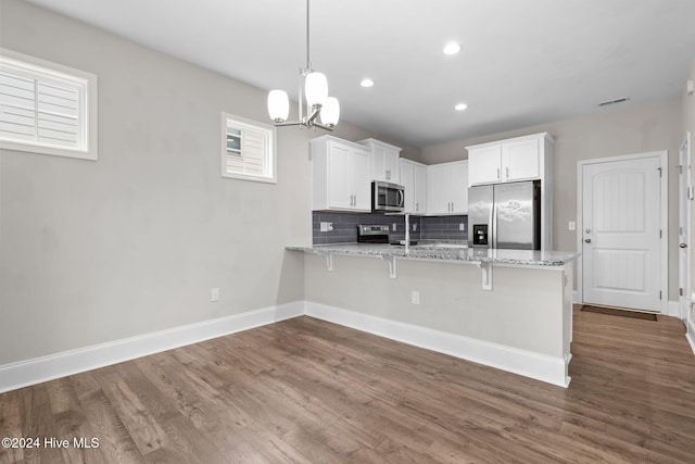 kitchen with white cabinets, hardwood / wood-style flooring, light stone countertops, appliances with stainless steel finishes, and decorative light fixtures