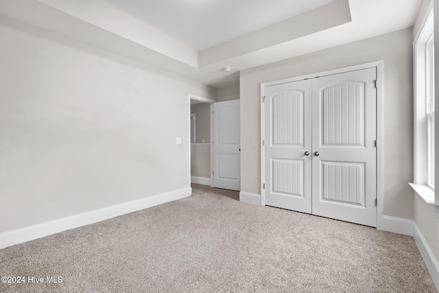 unfurnished bedroom featuring a tray ceiling, a closet, and carpet floors