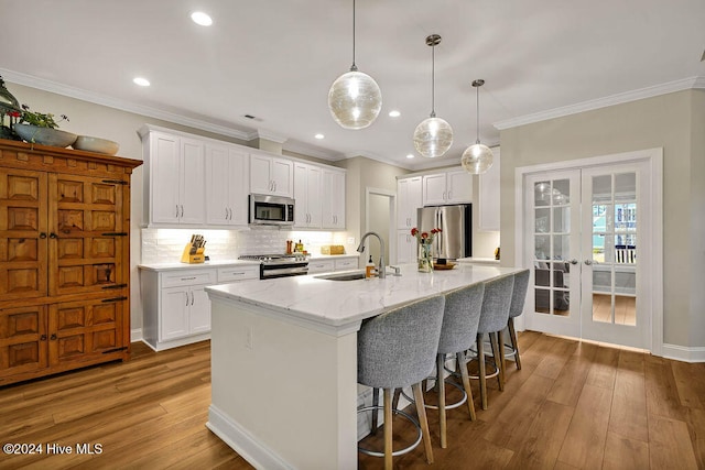 kitchen featuring french doors, stainless steel appliances, sink, white cabinetry, and an island with sink