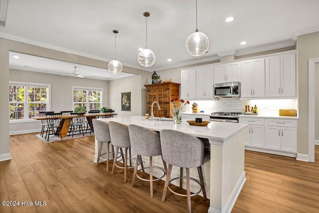 kitchen featuring white cabinets, appliances with stainless steel finishes, decorative light fixtures, and light hardwood / wood-style flooring