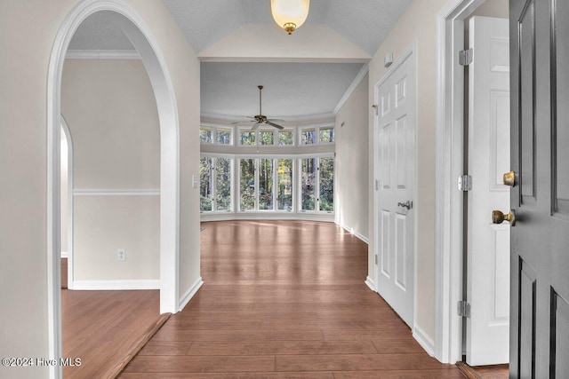 hallway featuring a textured ceiling, crown molding, dark wood-type flooring, and vaulted ceiling