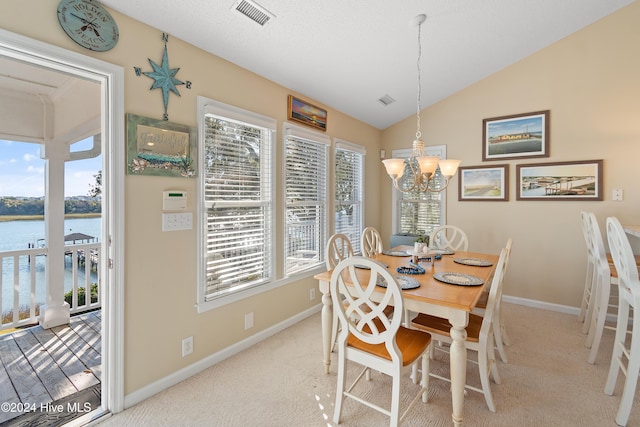 carpeted dining room featuring a notable chandelier, plenty of natural light, a water view, and lofted ceiling