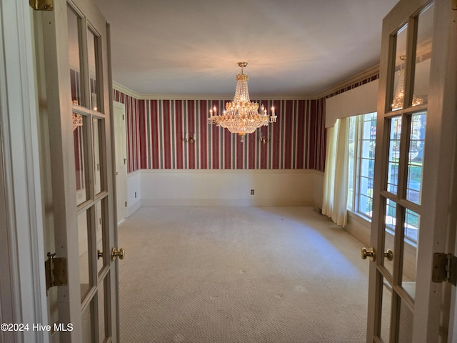 carpeted spare room with crown molding, french doors, and a notable chandelier