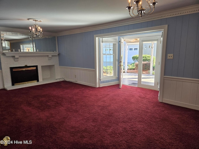 unfurnished living room featuring an inviting chandelier, carpet floors, crown molding, and a brick fireplace