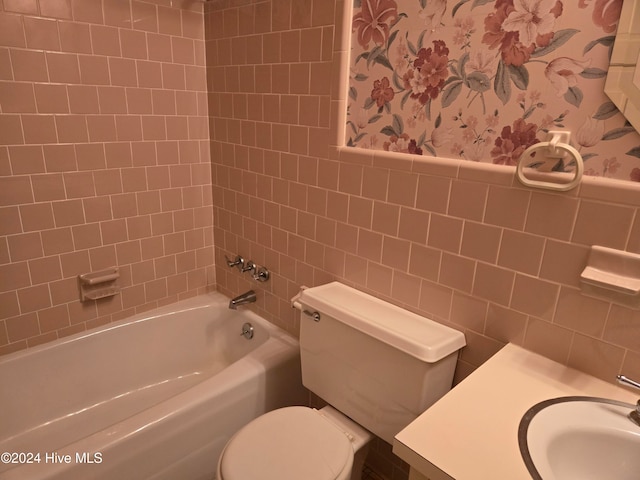 full bathroom featuring tiled shower / bath combo, toilet, tile walls, and sink