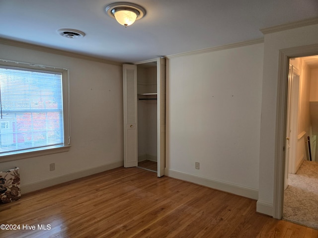 unfurnished bedroom featuring crown molding, a closet, and hardwood / wood-style flooring