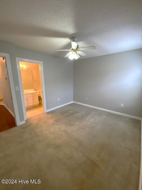 unfurnished bedroom with ceiling fan, carpet floors, a textured ceiling, and connected bathroom