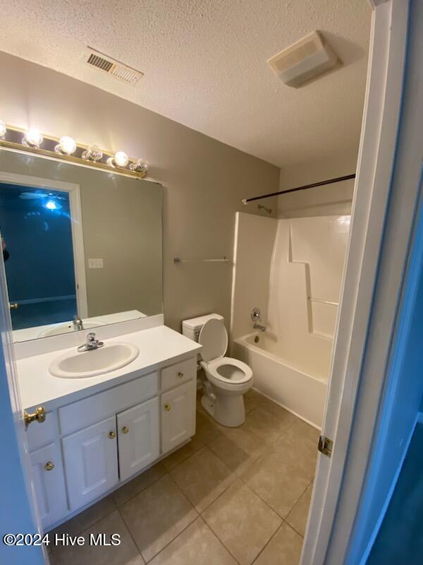 full bathroom featuring tile patterned floors, vanity, a textured ceiling, shower / washtub combination, and toilet