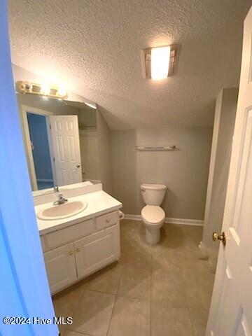 bathroom featuring tile patterned floors, vanity, a textured ceiling, vaulted ceiling, and toilet