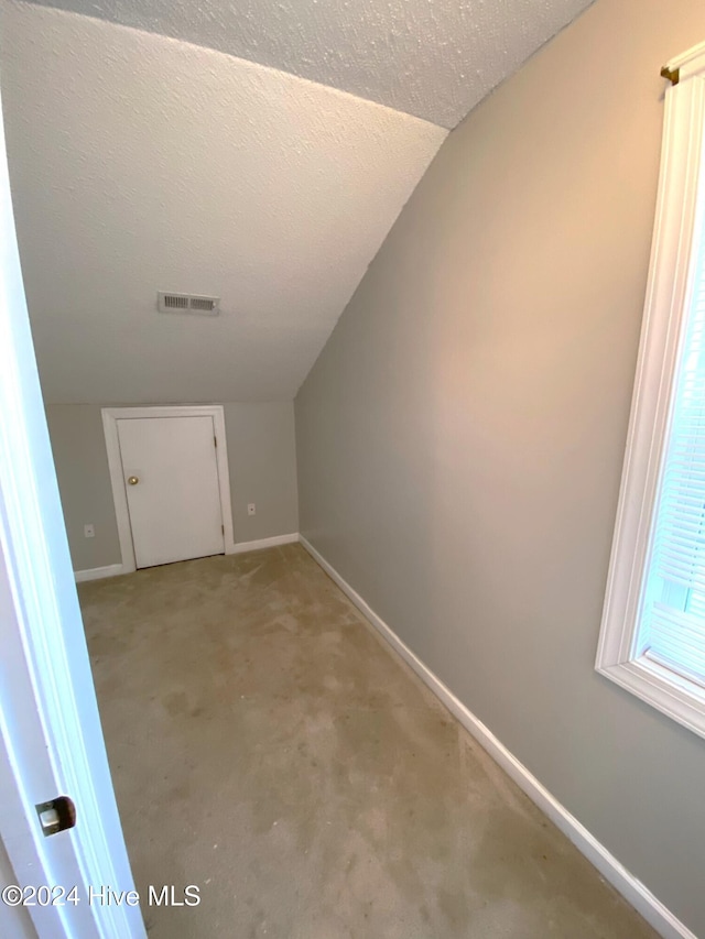 interior space with a textured ceiling and vaulted ceiling