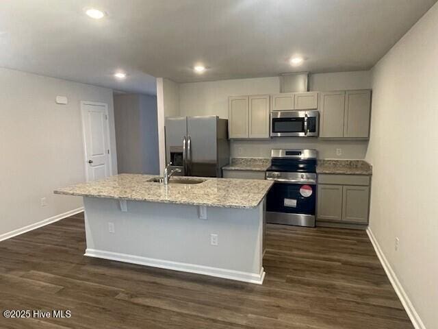 kitchen featuring light stone countertops, a center island with sink, gray cabinetry, and stainless steel appliances