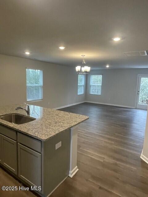 kitchen with light stone countertops, dark wood-type flooring, sink, hanging light fixtures, and a center island with sink