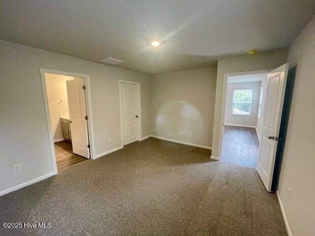 unfurnished bedroom with ensuite bath and dark colored carpet