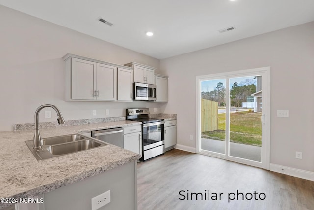 kitchen with kitchen peninsula, appliances with stainless steel finishes, light stone counters, sink, and light hardwood / wood-style floors