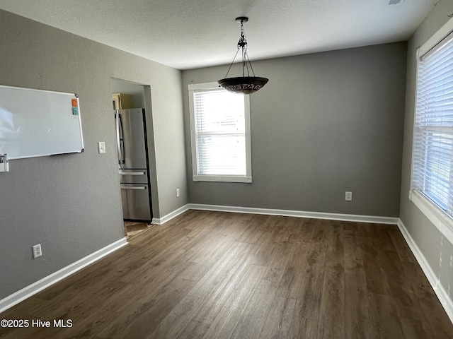 unfurnished dining area featuring a textured ceiling and dark hardwood / wood-style flooring