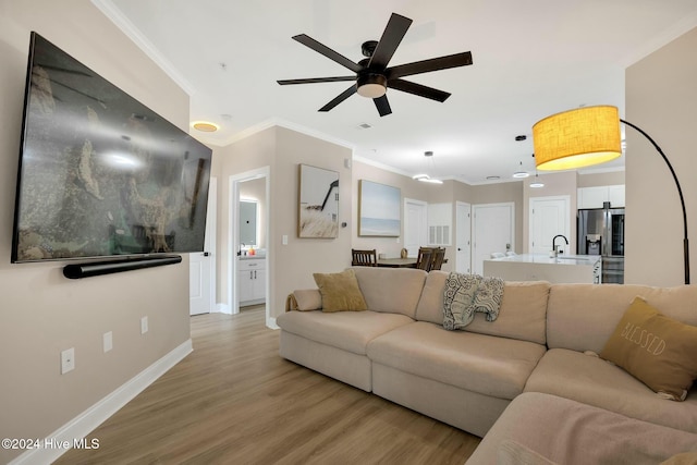 living room with ceiling fan, light hardwood / wood-style flooring, crown molding, and sink