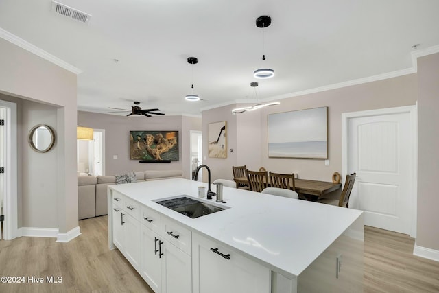 kitchen featuring pendant lighting, white cabinets, sink, ceiling fan, and an island with sink