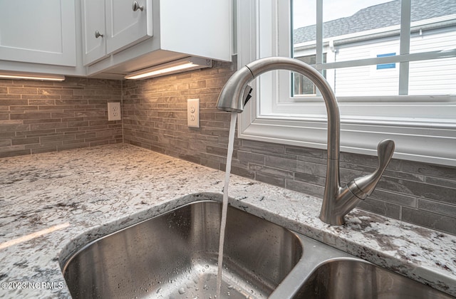 details with backsplash, white cabinetry, sink, and light stone counters